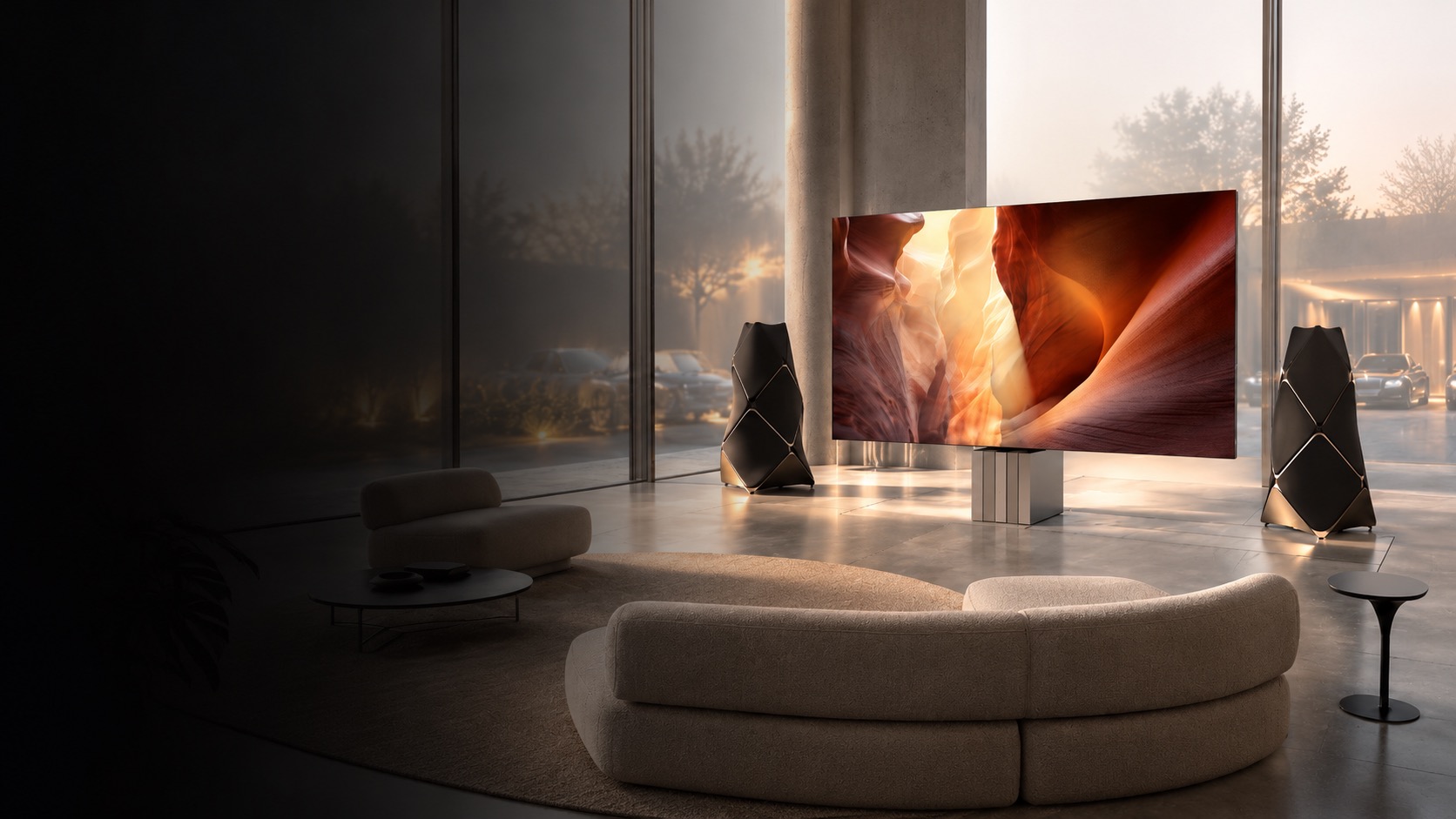 Concept render of a glass-walled living room at dusk with an outdoor courtyard and parked cars visible through the glass, a large television on a pedestal flanked by a pair of sculptural faceted floor-standing speakers intended to depict Beolab 90